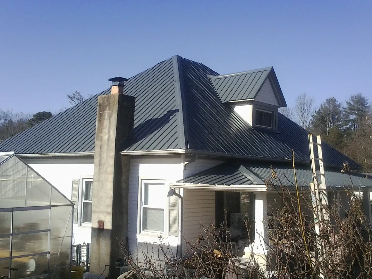 Dark blue standing seam metal roof on a white farmhouse with dormer — Slate & Tile Roof Repair by Roofing Brothers in Lyon Station
