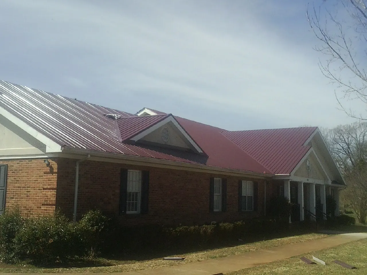 Red metal roof with gabled entries on a long brick building, from a Hail Damage Roof Repair job in Lyon Station
