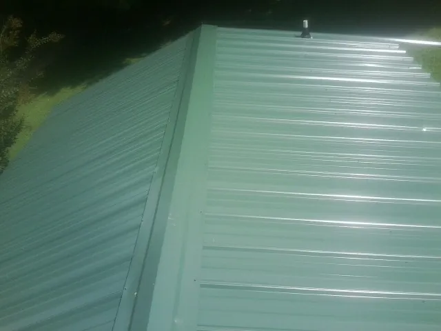 New green metal panels meeting at the ridge of a roof — Flat Roof Repair work by our crew in Lyon Station