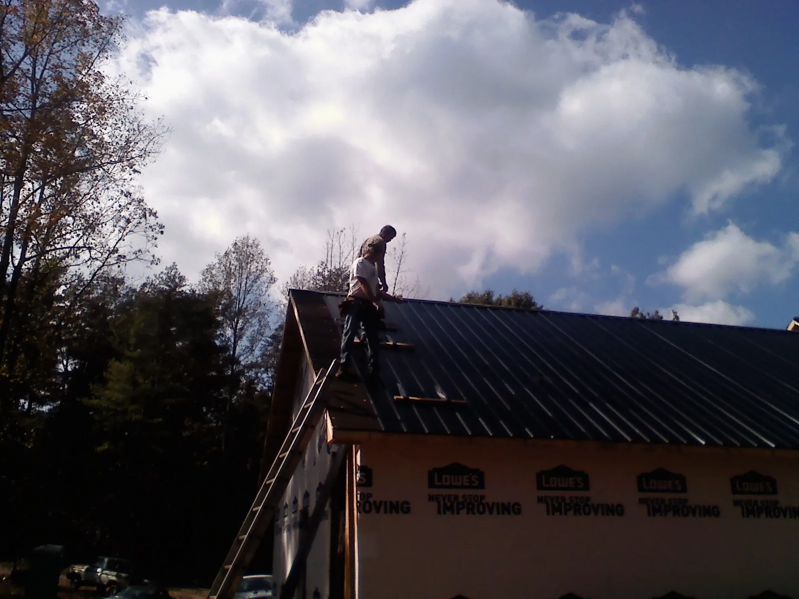 Roofer fastening dark metal panels high against a cloudy sky, from a Roof Inspection job in Lyon Station