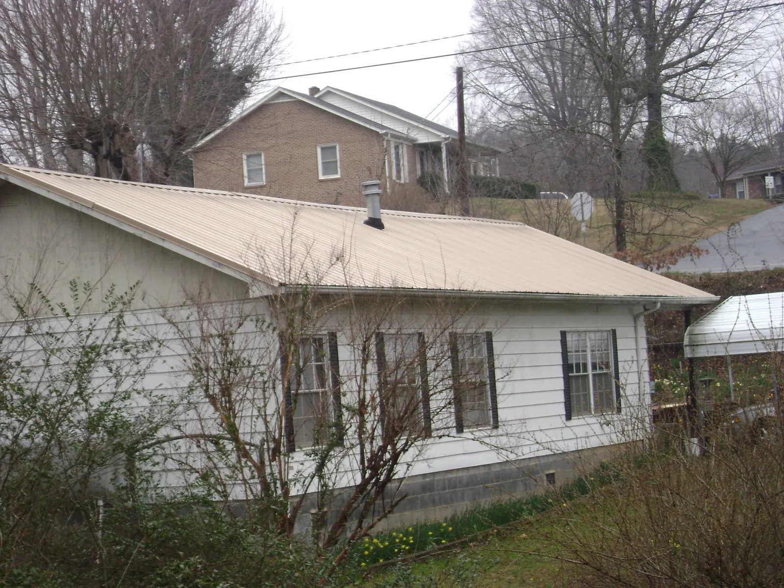 Tan metal roof on a white sided house set into a hillside — Commercial Roofing by Roofing Brothers in Lyon Station